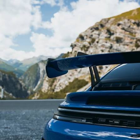 Heckfl&uuml;gel eines blauen Porsche GT3 vor Bergkulisse